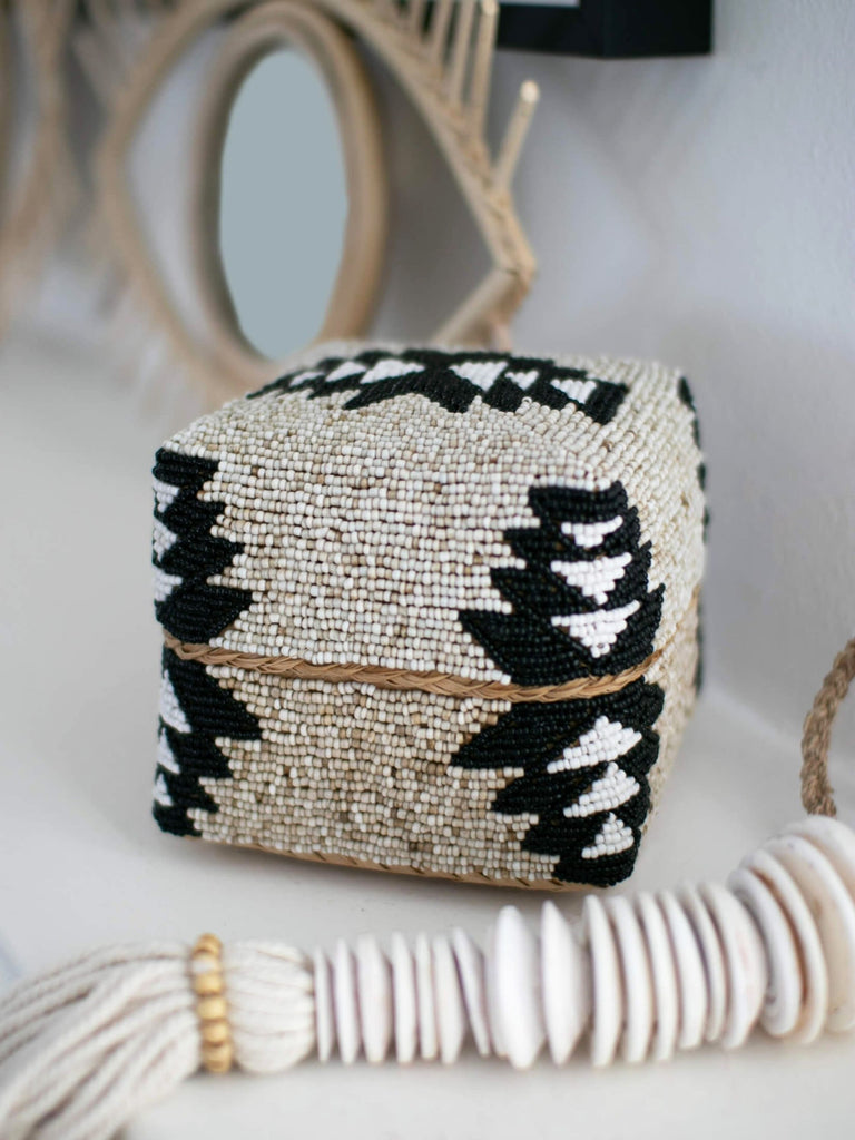 handmade beaded bamboo tribal basket on mantel next to shell disc stack tassel and rattan evil eye mirror