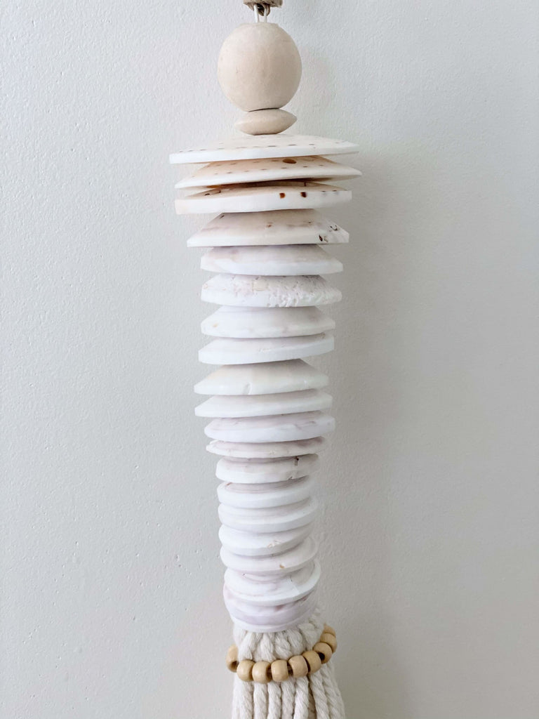 closeup of detail on stunning handmade white conus shell disc stack tassel hanging on white wall