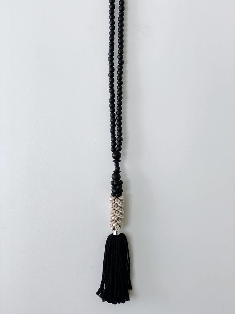 bohemian hand-carved black wooden bead tassel with beige shell cluster hanging on white wall
