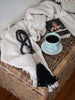 dark academia bohemian cozy vibes with black beaded shell cluster tassel next to cup of coffee and book