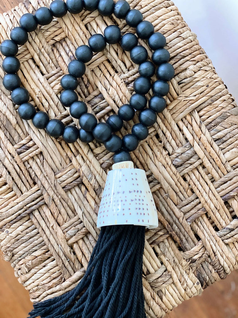 product photo of bohemian handcarved black wooden bead tassel with black conus shell on banana leaf placemat