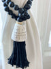 closeup of detail on handmade black wooden bead tassel with conus shell tied around white linen curtain