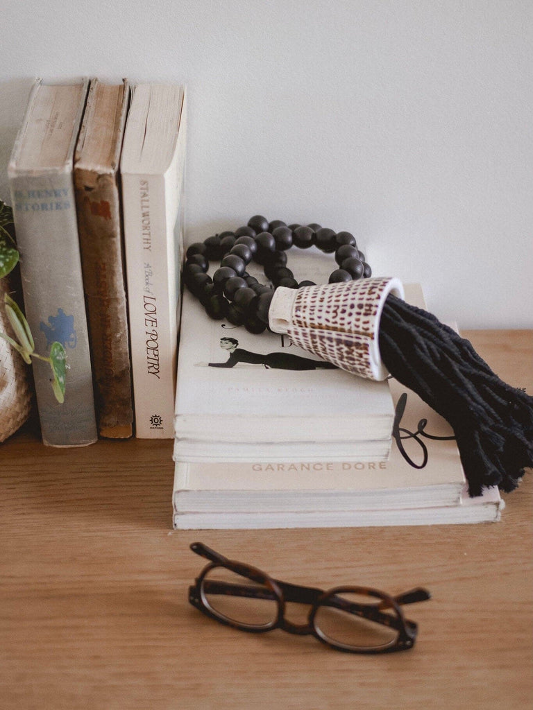 dark academia vibes with black wooden bead conus shell tassel on top of stacked books with glasses