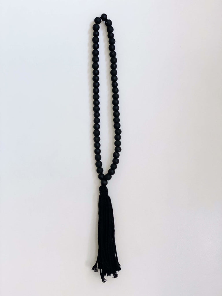 product photo of handcarved black wooden bead and black tassel hanging on white wall