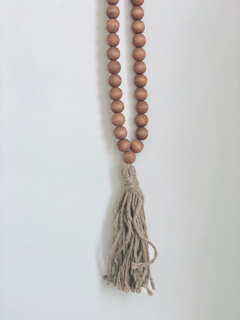 bohemian handcarved brown wooden bead jute tassel hanging on white wall