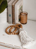 light academia vibes with boho wooden bead conus shell tassel next to plants, books, and candle on white dresser