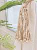 handmade wooden bead tie-back tied around a white linen curtain next to small palm leaf tree