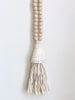 closeup product photo of handcarved natural boho wooden bead conus shell tassel hanging on white wall
