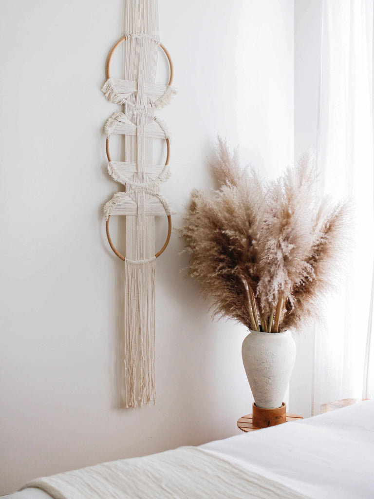 handmade rattan ring trio woven wall hanging with pampas in a light filled modern bohemian bedroom